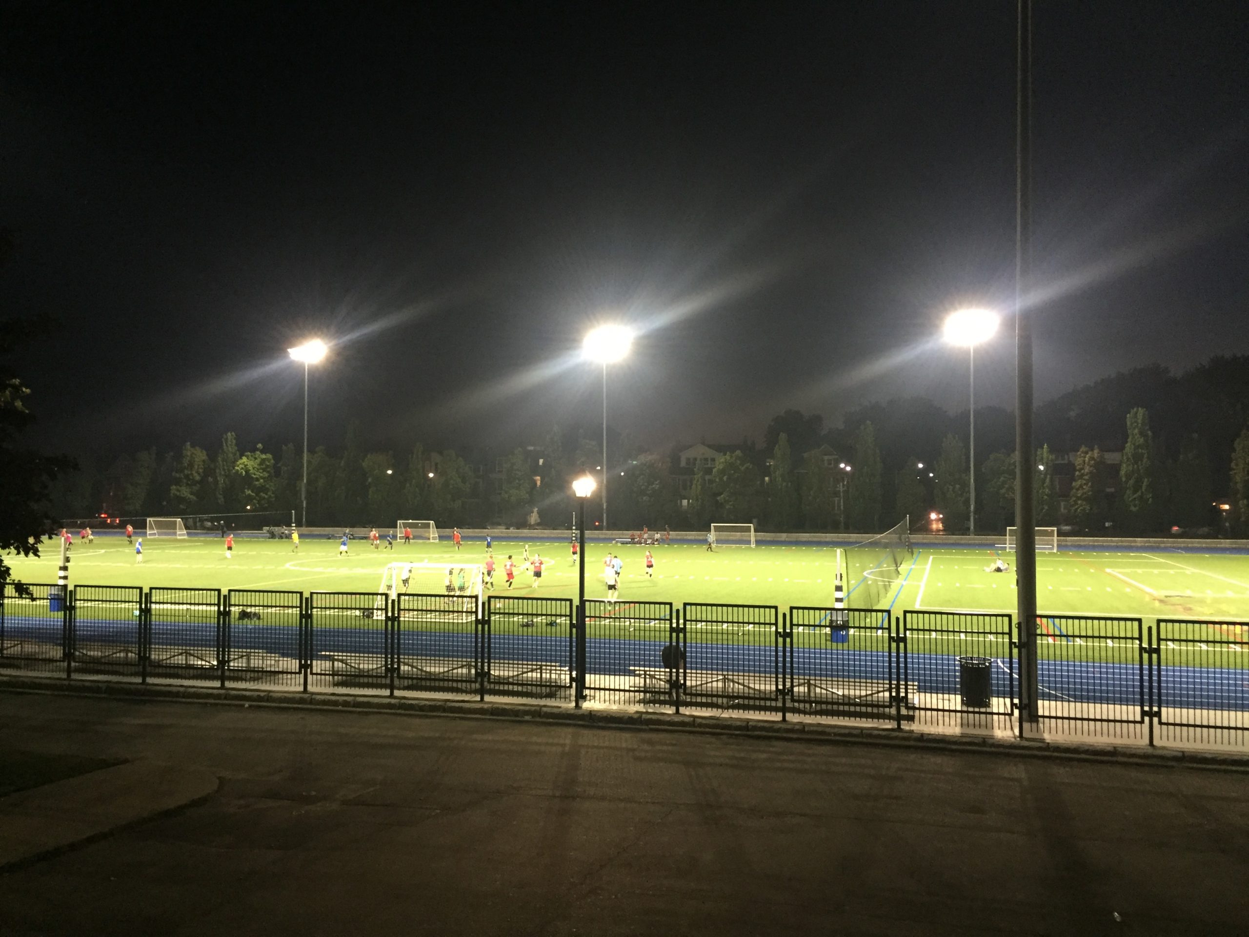 People playing soccer in the field at night.