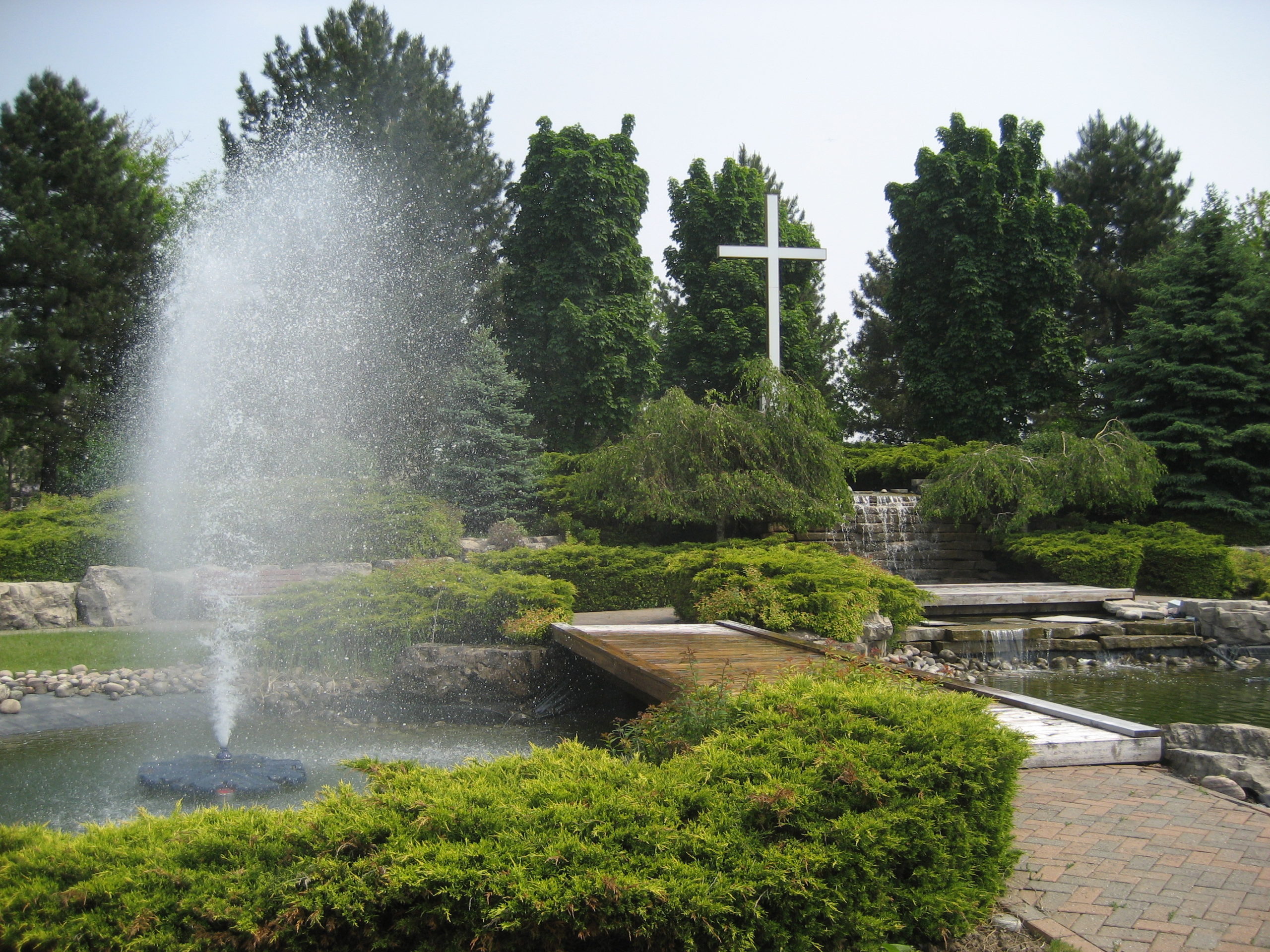 Pond with water spout surrounded by hedges and trees